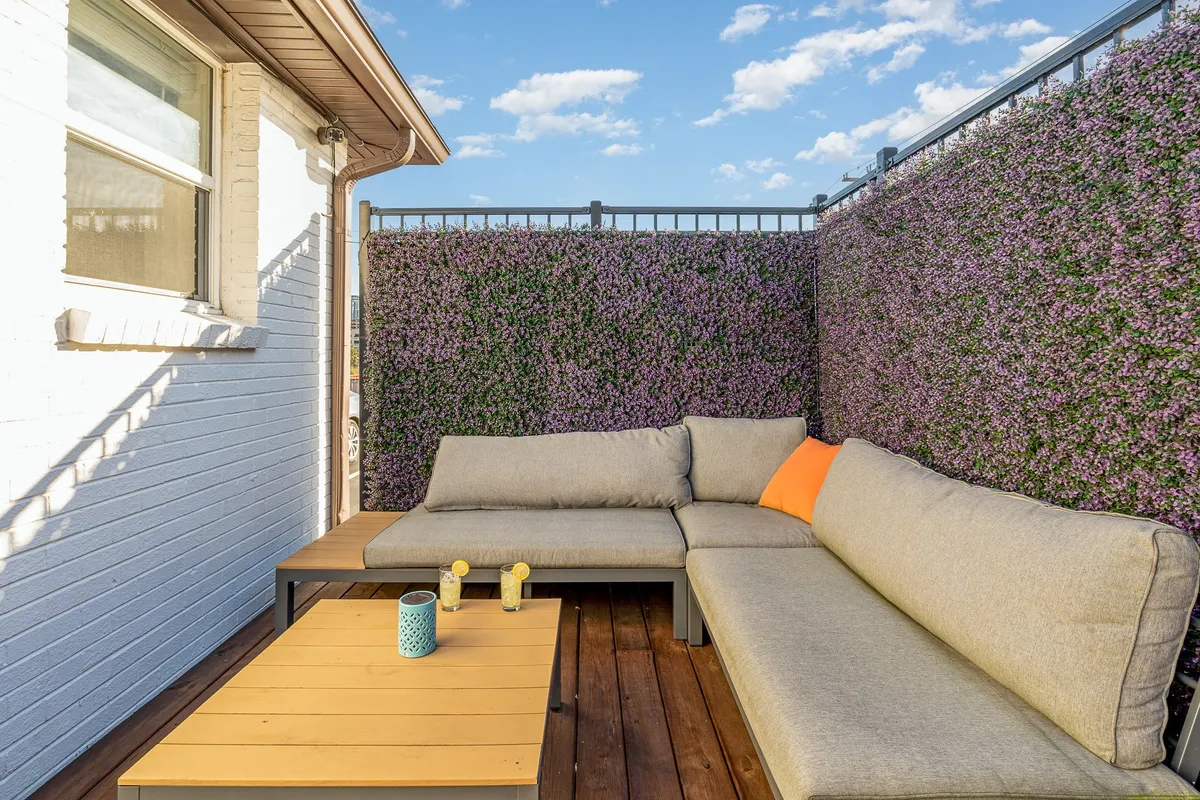This image showcases a comfortable, fenced patio with a plush sectional sofa adorned with decorative cushions and a coffee table. The setting exudes relaxation and intimacy, ideal for unwinding or enjoying a quiet morning coffee. The warm glow of sunset emphasizes the patio's tranquil and private atmosphere.