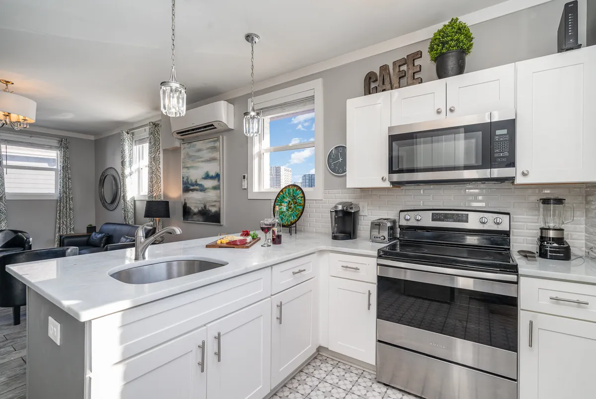 A modern, cozy kitchen with a prominent island featuring bar seating for three, stainless steel appliances, decorative wall art, and a window that offers a city view. The setup is perfect for cooking, entertaining, and relaxed social gatherings.