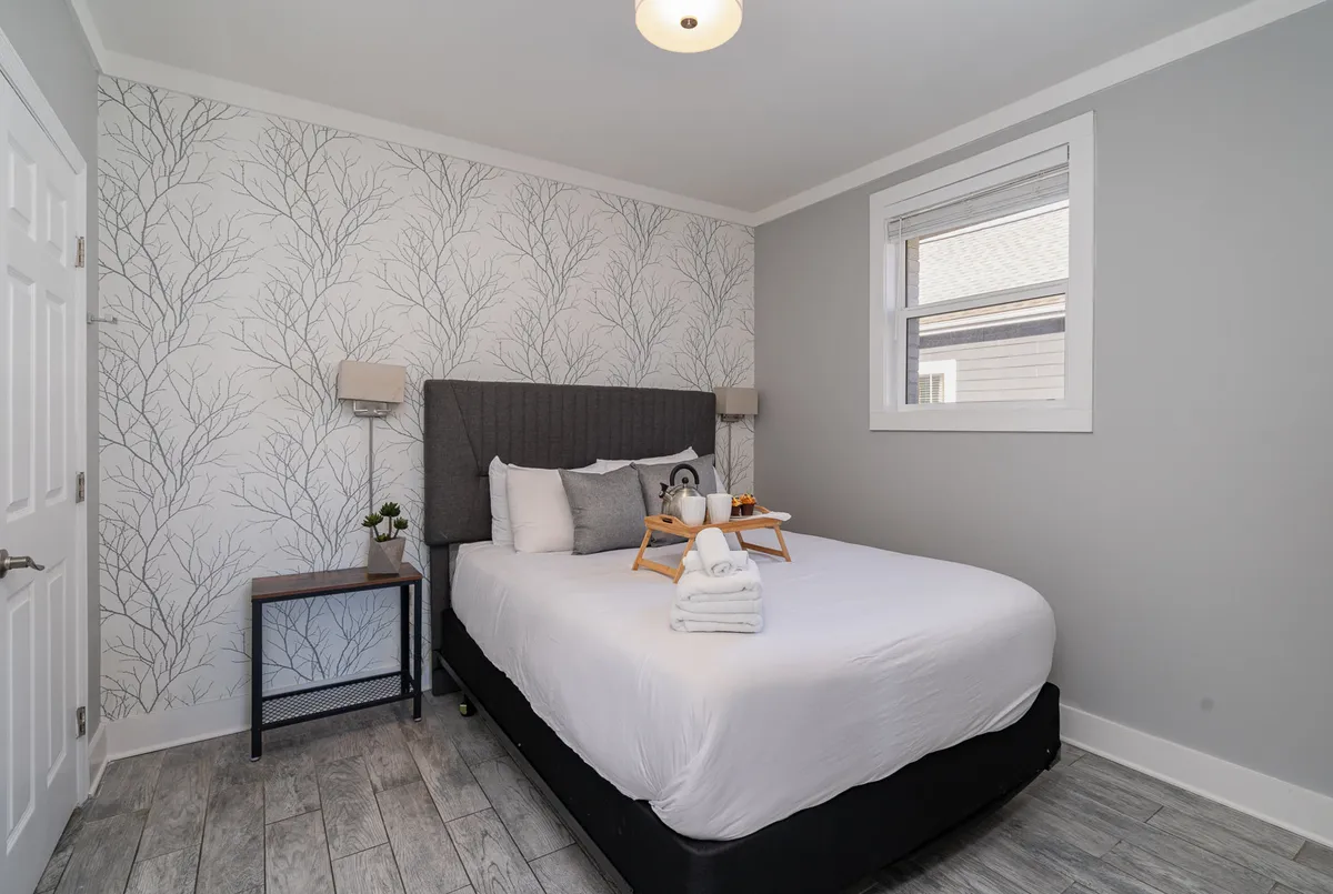 A serene bedroom featuring a comfortable bed, a decorative accent wall, and a side table with a tray, capturing a peaceful atmosphere ideal for restful sleep and relaxation.